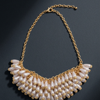 A gold-tone statement necklace featuring cascading rows of white faux-pearl teardrop beads, displayed on a dark textured background.