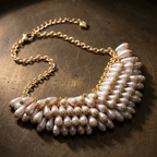 A statement collar necklace featuring white pearl-like beads and gold-toned metal details, displayed on a dark textured metallic surface.