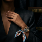 A close-up lifestyle shot of a model wearing a patterned silk scarf bracelet tied around their wrist, paired with a dark navy blazer.