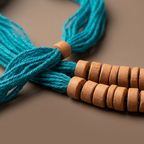 A close-up of a braided turquoise blue cord or strap with several round light brown wooden beads arranged in two rows on a smooth taupe-brown background.