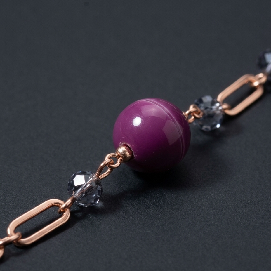 A close-up of a jewelry chain bracelet featuring a prominent glossy purple bead, rose gold paperclip links, and clear faceted crystal beads on a dark gray background.