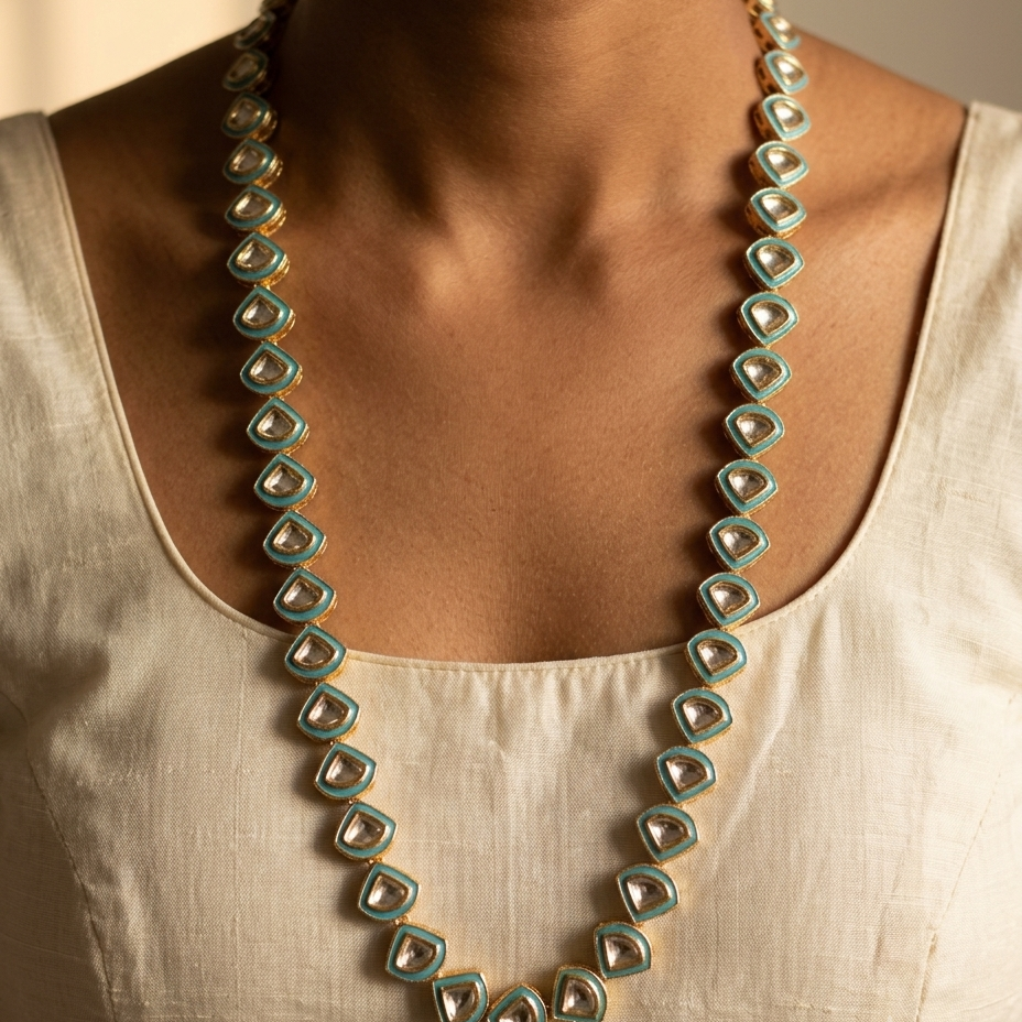 A close-up of a model wearing a long statement necklace made of repeating turquoise and gold geometric beads over a cream-colored linen top.