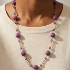 A close-up of a model wearing a multi-strand beaded necklace with purple beads, gray marbled beads, and rose gold metal links over a cream knit sweater.