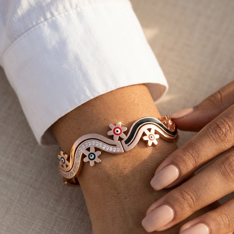 A close-up of a person's wrist wearing a decorative wavy cuff bracelet. The bracelet has a rose gold base with black enamel sections, white floral motifs, and small colorful circular accents.
