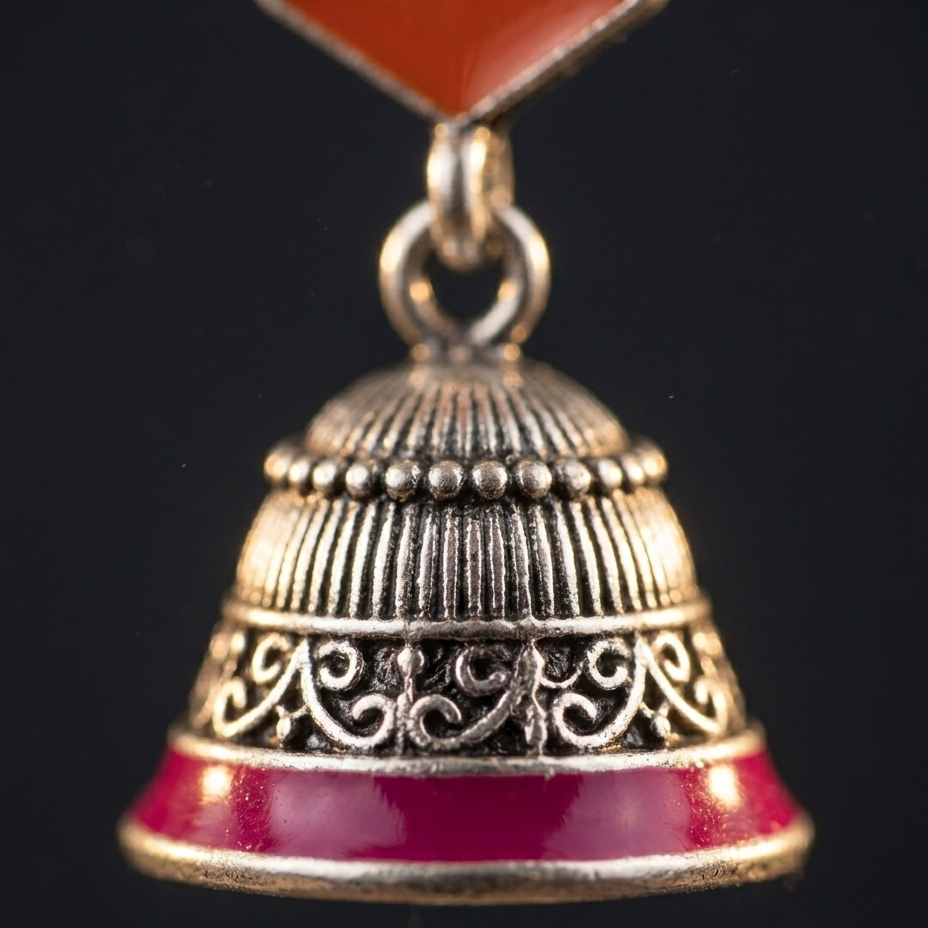 A close-up of a traditional Indian Jhumka earring featuring a silver-toned bell with red enamel detailing and a red stone at the top, set against a solid black background.