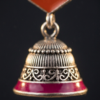 A close-up of a traditional Indian Jhumka earring featuring a silver-toned bell with red enamel detailing and a red stone at the top, set against a solid black background.