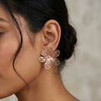 A close-up of a woman's ear wearing a rose gold flower-shaped stud earring with intricate wire detailing.