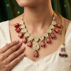 A close-up of a woman wearing a gold-plated statement necklace with red and white marbled beads, set against a dark green background.