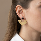 A close-up side profile of a woman wearing a gold crescent-shaped dangle earring with a small black stone stud, against a neutral beige background.