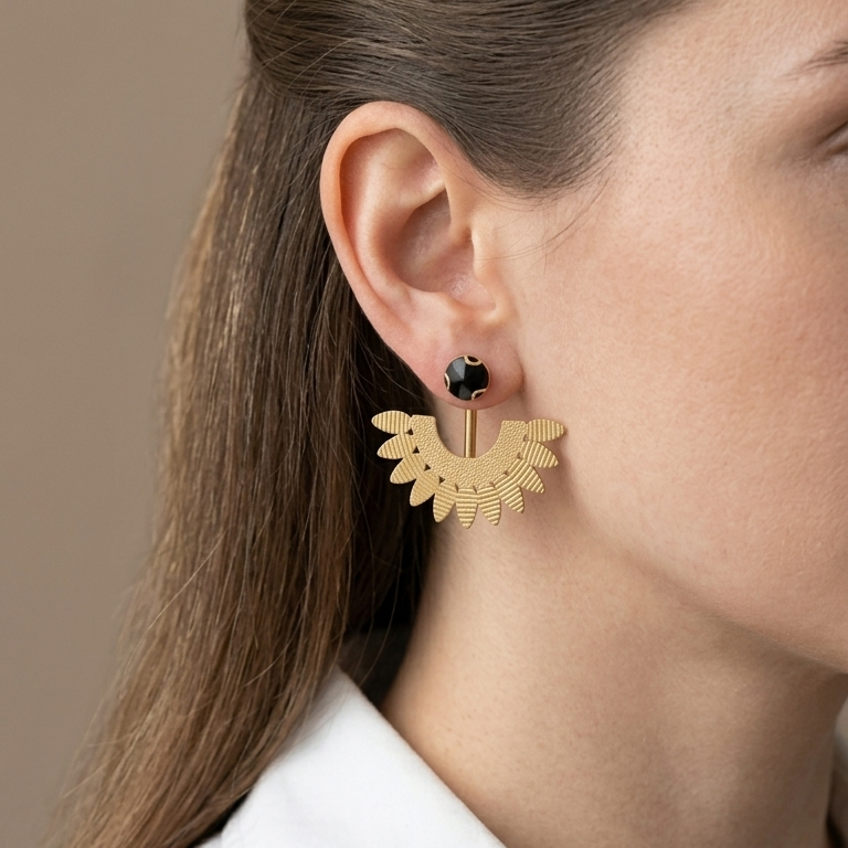 A close-up side profile of a woman wearing a gold crescent-shaped dangle earring with a small black stone stud, against a neutral beige background.