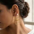 A close-up side profile of a woman wearing a gold wire flower dangle earring with a single white pearl stud above it.