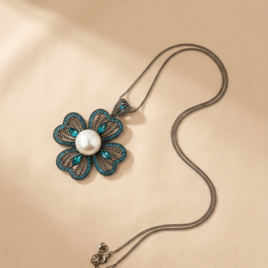 A floral pendant necklace with a central white pearl surrounded by teal and silver filigree petals, resting on a warm beige textured background.