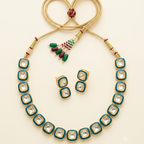 A gold-plated jewelry set featuring a necklace and matching earrings with square-cut clear stones bordered by teal green enamel and gold frames, arranged on a light cream background.