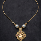 A gold-tone chain necklace with two white pearl-like beads and an ornate central pendant featuring a large clear faceted stone and small purple stones, displayed on a dark textured background.