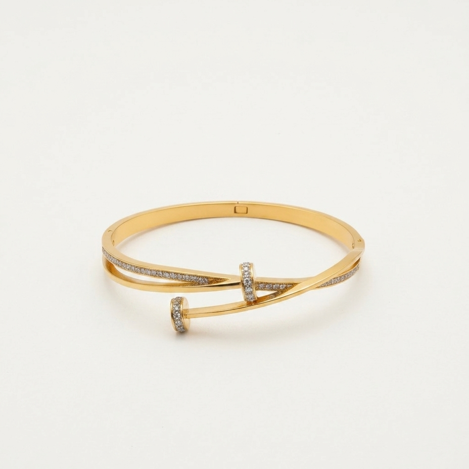 A gold hinged bangle bracelet with a twisted cross design, accented with small pavé-set clear stones, photographed on a clean white background.