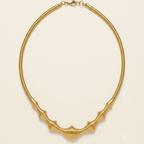 A gold snake chain necklace with a textured, ribbed bat-wing or wing-like centerpiece, displayed on a clean, solid cream background.