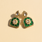 A pair of gold-plated kundan earrings with vibrant green enamel inlay, a central white pearl, and a teardrop-shaped clear stone at the top, displayed on a warm beige background.