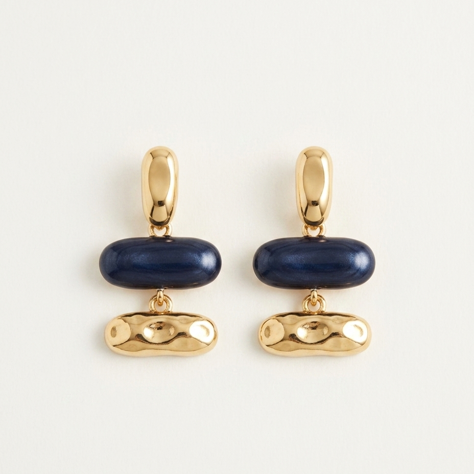 A pair of gold-tone drop earrings with a smooth dark blue oval centerpiece and a textured gold drop below, displayed on a clean off-white background.