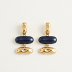 A pair of gold-tone drop earrings with a smooth dark blue oval centerpiece and a textured gold drop below, displayed on a clean off-white background.