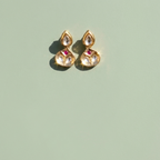 A pair of gold-toned Indian jhumka earrings with clear teardrop crystals and small pink gemstone accents, displayed on a solid sage green background.