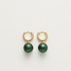 A pair of gold huggie hoop earrings with dangling dark green pearl-like drops, shown on a clean off-white background.