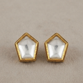 A pair of gold pentagonal stud earrings with clear faceted dome-cut stones, displayed on a textured beige surface.