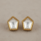 A pair of gold pentagonal stud earrings with clear faceted dome-cut stones, displayed on a textured beige surface.