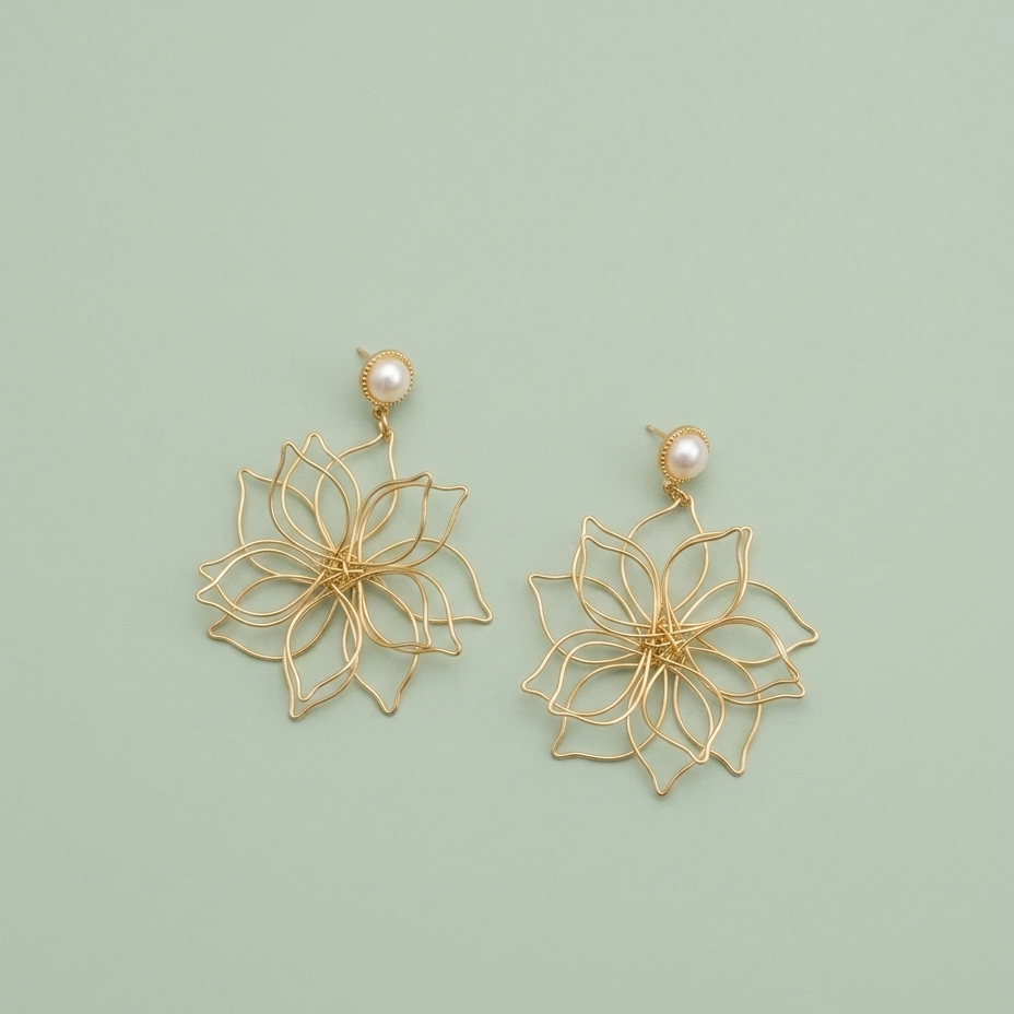 A pair of gold wire flower dangle earrings with small white pearl studs, displayed on a solid pale green background.