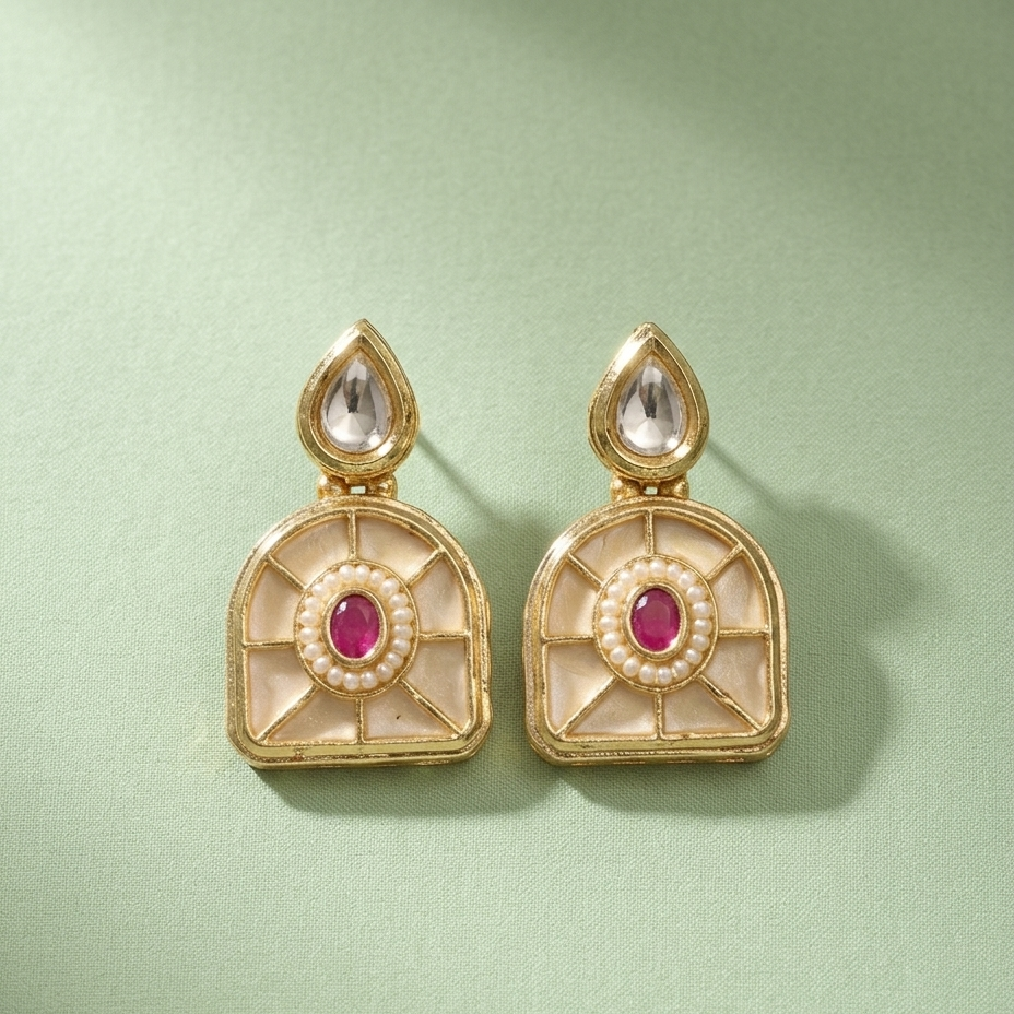 A pair of ornate gold-toned earrings with cream inlay, small pearl-like borders, oval pink centers, and clear teardrop stones, arranged on a pale green background.