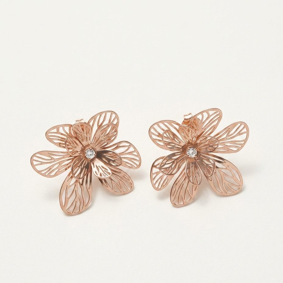 A pair of rose gold flower-shaped stud earrings with delicate filigree petals and a small clear crystal in the center, displayed on a clean off-white background.