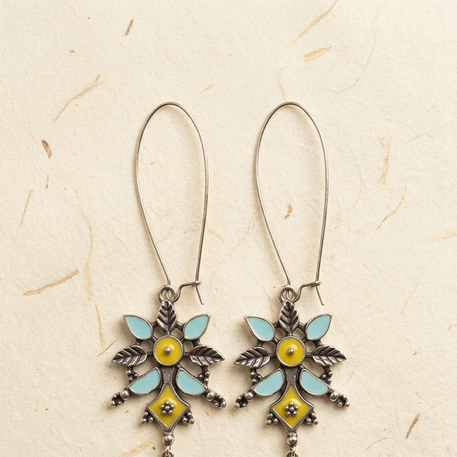 A pair of silver-toned dangle earrings with light blue enamel leaf-like wings, yellow enamel centers, and dangling yellow and blue accents, displayed on a textured beige background.