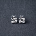 A pair of silver geometric stud earrings with pavé-set clear stones, displayed on a textured dark gray fabric background.