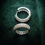 A pair of silver hoop earrings covered in small clear stones, with one earring showing the front and the other showing the back closure, placed on a dark green velvet background.