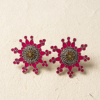 A pair of snowflake-shaped stud earrings with vibrant pink enamel, gold-toned central details, and silver-toned outer borders, displayed on a textured beige surface.