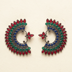 A pair of traditional Indian silver-toned earrings decorated with red, green, and blue stones, displayed on a textured off-white paper background.