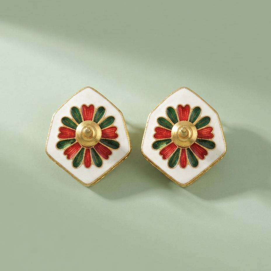 A pair of white enamel hexagonal stud earrings with a gold-tone center and red and green petal details, displayed on a soft sage green background.