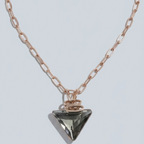 A rose gold chain necklace with a faceted triangular pendant, displayed on a light gray background.
