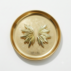 A round gold-toned metal tray with a raised decorative border and a symmetrical leaf-like motif in the center, photographed from above on a plain white background.