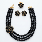 A three-piece black and gold jewelry set featuring a double-strand beaded necklace, a matching flower-shaped collar, and two matching flower-shaped earrings, displayed on a clean white background.