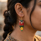 Close-up of Dhaṭṭī cylindrical terracotta folk art earrings with red body, black arch border, petal motifs and yellow clay teardrop drop — artisan jewellery by House of Yugavi India