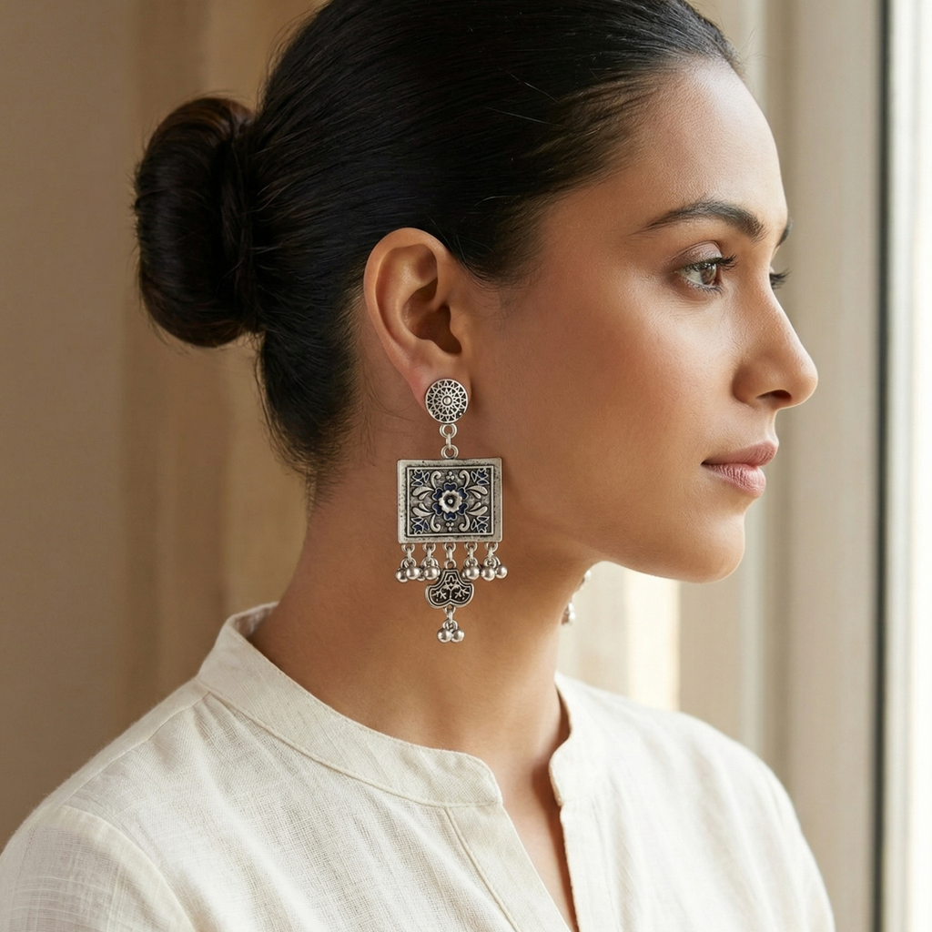 Close-up of Yugavi Arita meenakari rectangle — ivory cream enamel ground with navy blue scrolling arabesque arms radiating from centre, white five-petal flower with navy blue centre stone, small leaf forms at corners, oxidised silver border, Mughal tile and Jaipur blue pottery inspired enamel design