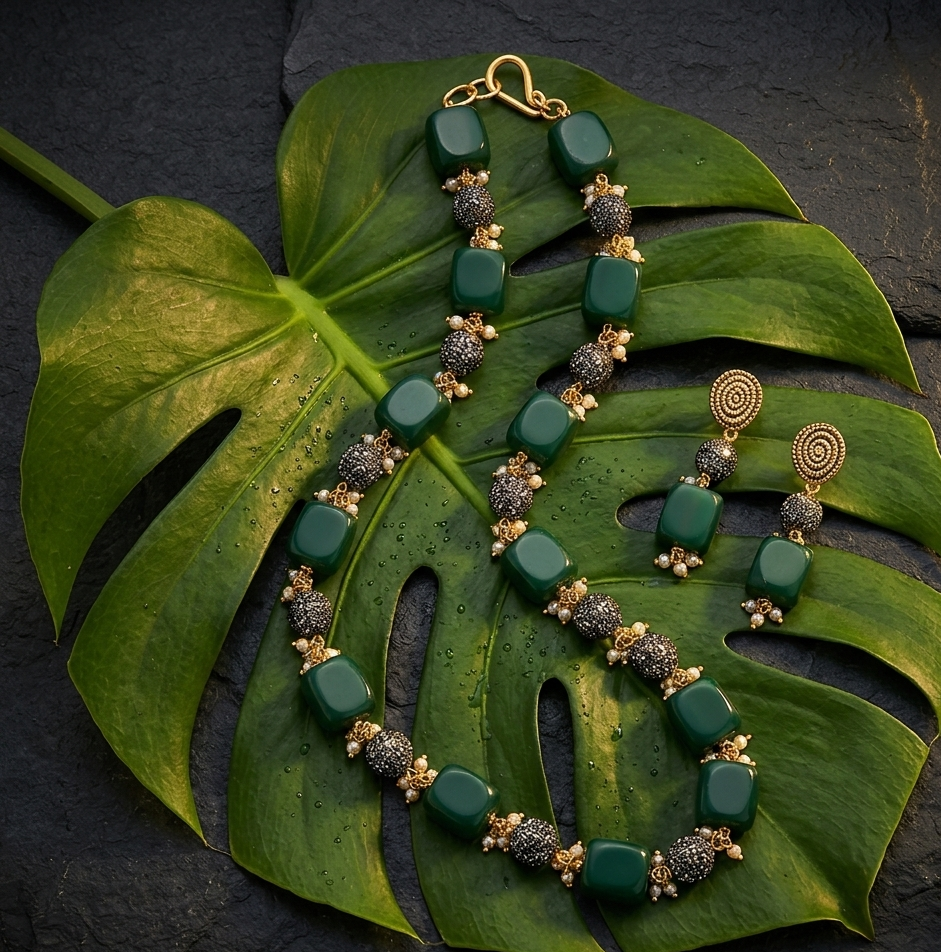 Green and gold jewelry set on a large green leaf against a dark background