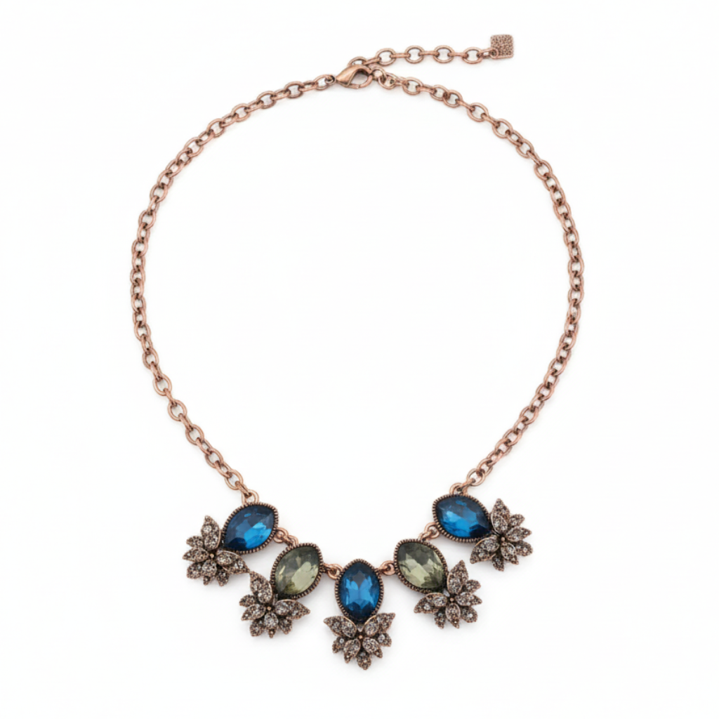 Close-up of Yugavi Kshanika stone V-composition — deep sapphire blue faceted teardrop and marquise stones beside olive-sage green oval faceted stones set in rose gold bezels, with pavé champagne crystal flower clusters surrounding, showing the three-colour stone palette