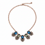 Close-up of Yugavi Kshanika stone V-composition — deep sapphire blue faceted teardrop and marquise stones beside olive-sage green oval faceted stones set in rose gold bezels, with pavé champagne crystal flower clusters surrounding, showing the three-colour stone palette