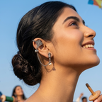 Woman with stylish earrings looking up at kites against a blue sky
