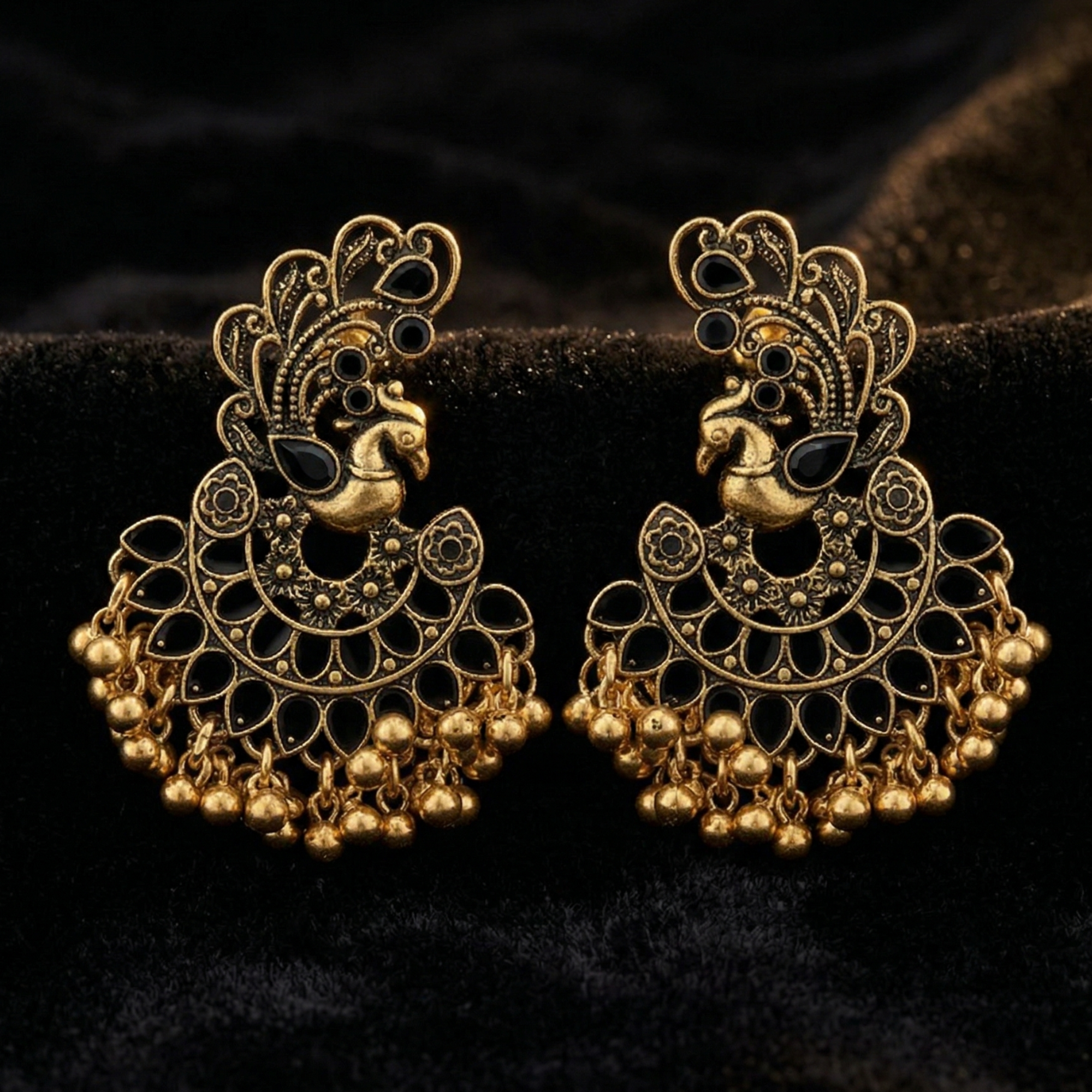 Close-up of Yugavi Priyana earring peacock motif — antique gold open-work Mayura with black oval cabochon feather stones, rising crest scroll and detailed bird body, temple jewellery heritage design