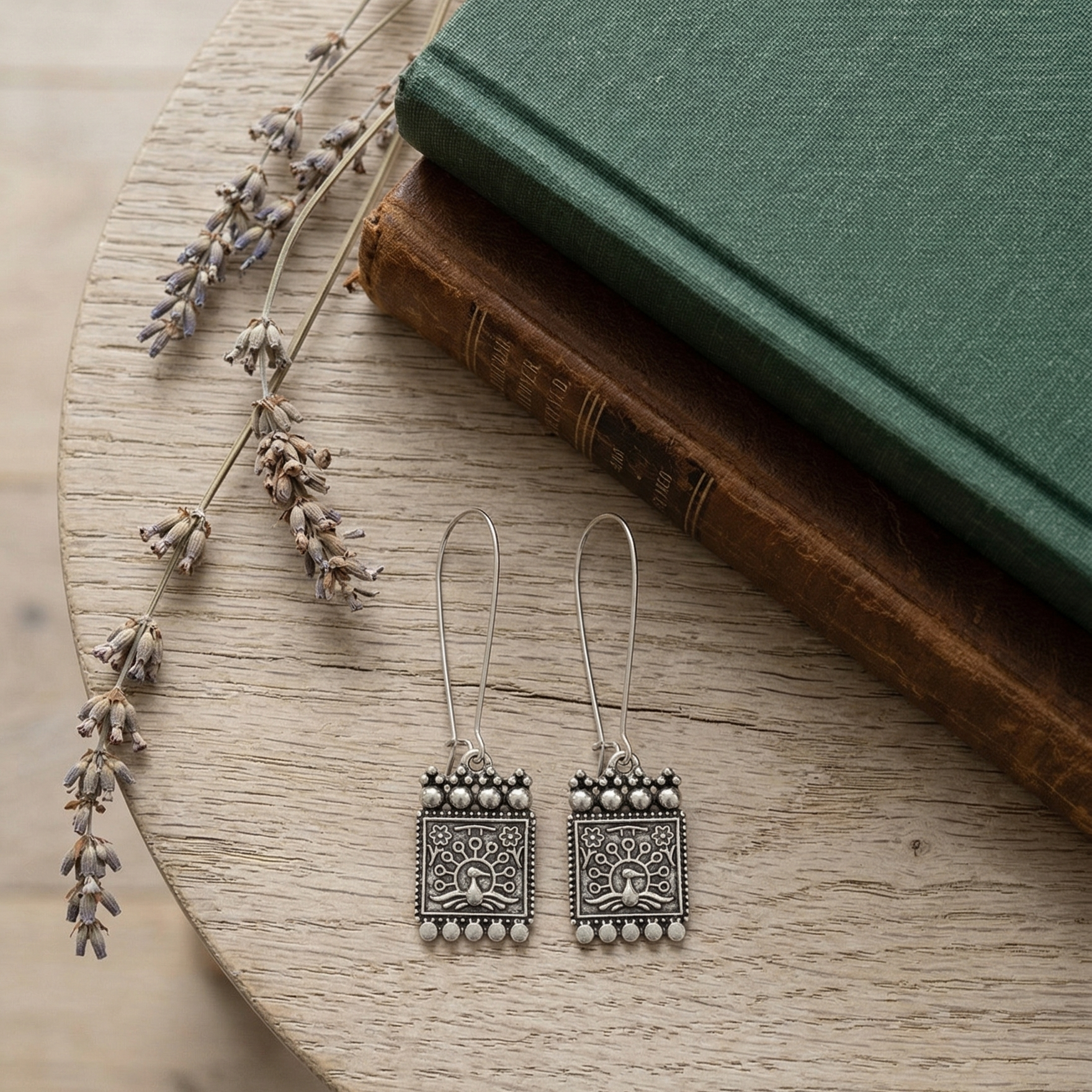 Close-up of Yugavi Raksha tablet engraving — oxidised silver relief showing peacock with spread tail at base, symmetrical tree of life branches rising above with flower tips, six-petal flower motifs in upper corners, dot-bead border frame, Indian folk art design