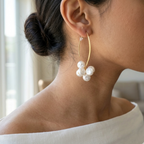 Close-up of a woman wearing gold hoop earrings with pearls indoors.
