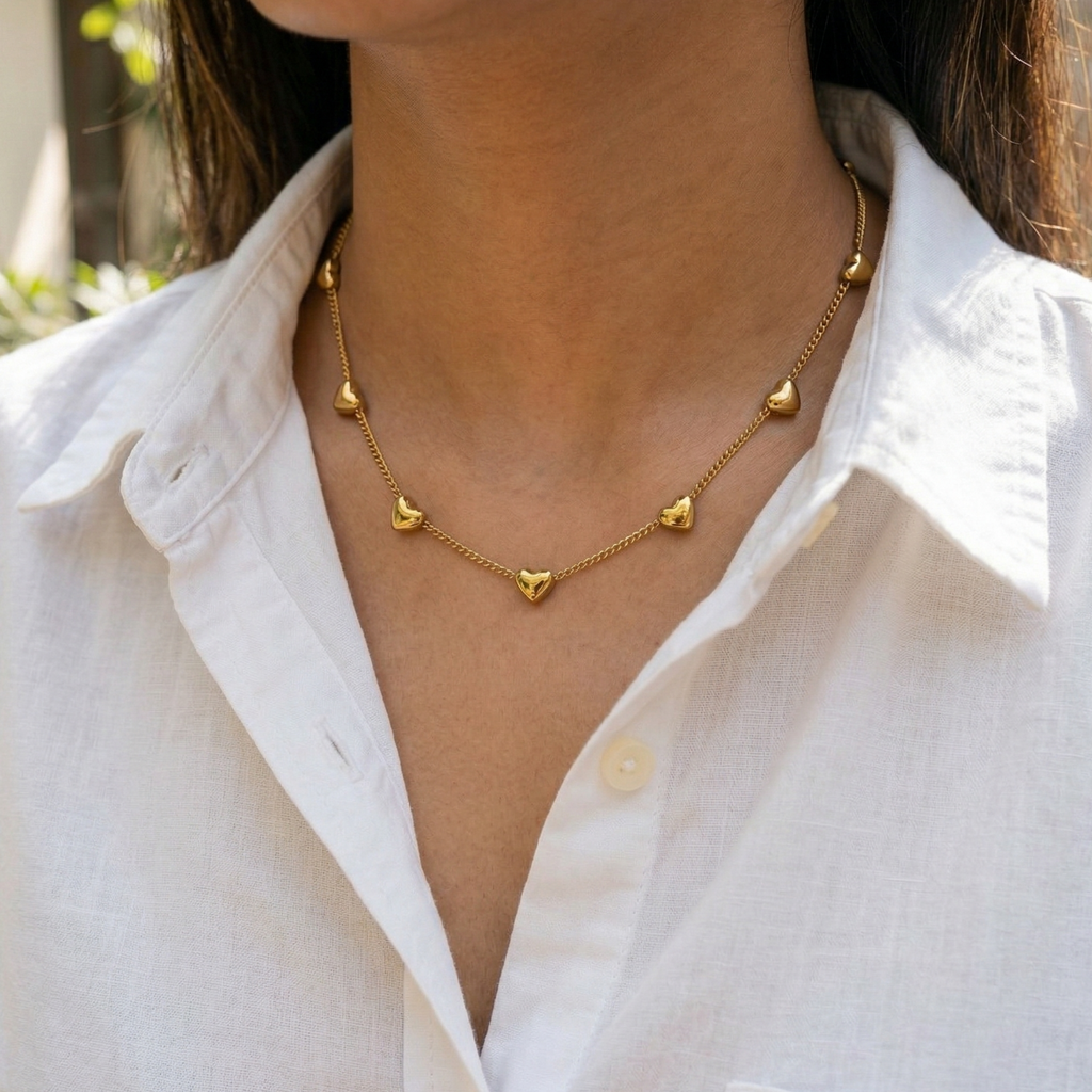 Close-up of Yugavi Saisha necklace showing individual puffy 3D gold heart charms on fine cable chain — polished solid gold heart forms catching light, bright gold finish, delicate chain station necklace detail