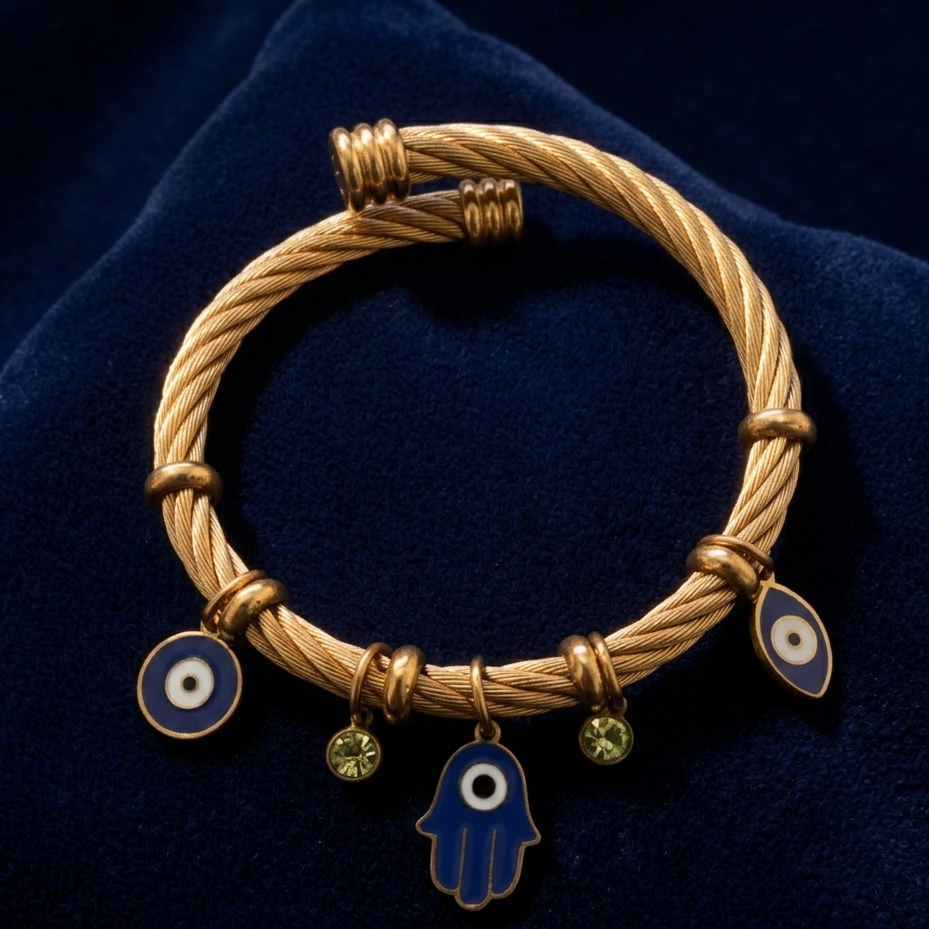 Gold bracelet with evil eye and Hamsa charms on a dark blue fabric background
